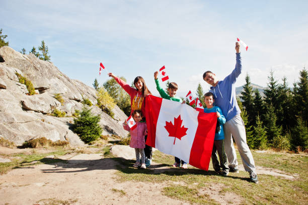 A family of 5 taking a photo behind the Canadian flag